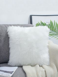 a white fluffy pillow sitting on top of a gray couch next to a green plant