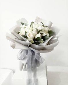 a bouquet of white flowers in a clear vase with ribbon around the bottom and green leaves on top