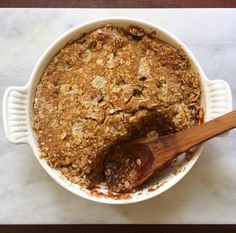 a wooden spoon sitting in a white bowl filled with baked oatmeal crumbles