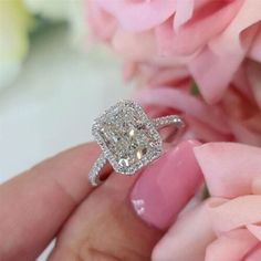 a close up of a person's hand with a ring on it and flowers in the background