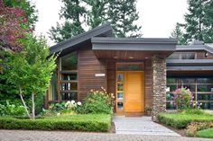 a house that is in the middle of some bushes and flowers on the front lawn