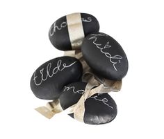 four black rocks with white writing on them tied to a ribbon and placed in front of a white background