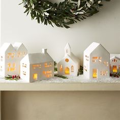 three white houses are sitting on a shelf with candles in the windows and greenery around them