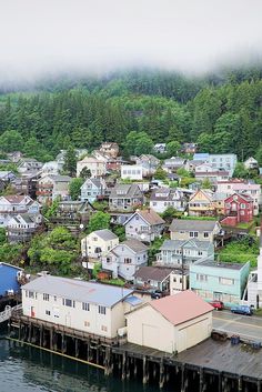 an aerial view of houses on the water with fog in the air and trees behind them