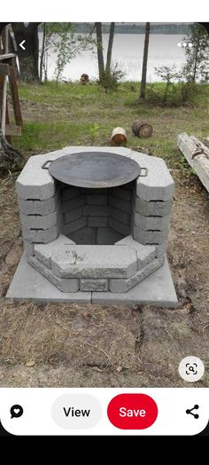 an outdoor fire pit in the middle of a field with trees and water behind it