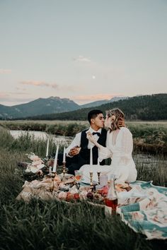 a newly married couple sitting on a blanket in the middle of a field at sunset