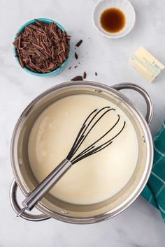 a pot with chocolate and whisk in it sitting on a table next to other ingredients