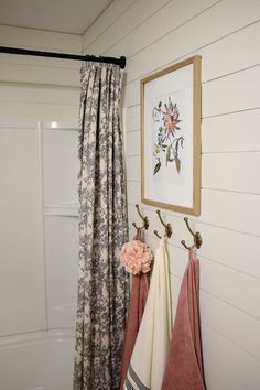 two towels hanging on hooks in front of a shower curtain and flowered towel rack