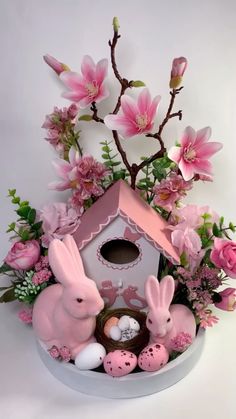 a birdhouse filled with pink flowers and easter eggs next to two bunny figurines