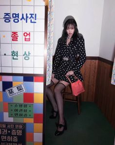 a woman sitting on top of a wooden chair in front of a colorful tiled wall