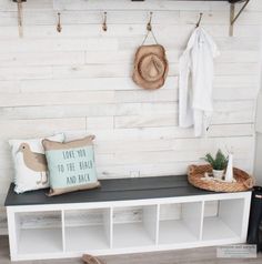 a bench that has some pillows on it next to a coat rack and hat rack