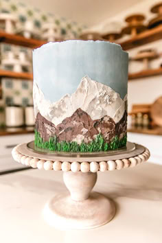 a cake decorated with mountains and grass on top of a white table in a kitchen