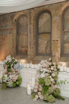 two vases filled with flowers and candles next to each other in front of windows