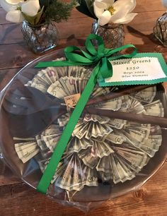 a glass platter with money in it on top of a wooden table next to flowers