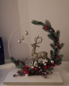 a christmas wreath with ornaments and deer in it on top of a white table next to a black speaker