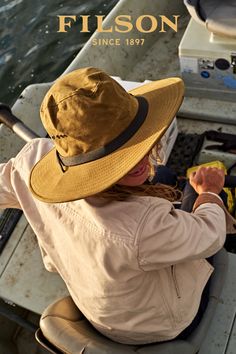 a woman sitting in a boat on the water wearing a hat and holding a fishing rod