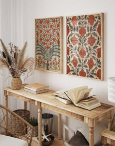 two paintings hanging on the wall above a wooden table with books and plants in front of it