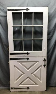 an old white door with glass and metal bars on the bottom, in front of a gray wall