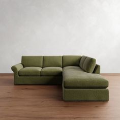 a large green couch sitting on top of a wooden floor next to a white wall