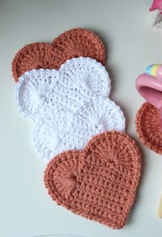 two crocheted heart shaped dishes next to a pink and yellow spoon holder on a white surface