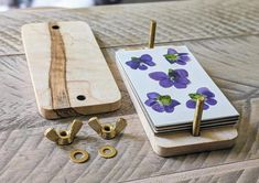 a wooden board with purple flowers on it next to some brass screws and nuts