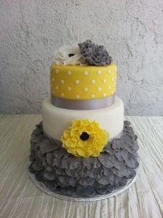 a three tiered cake with yellow flowers and gray ruffles on it's side