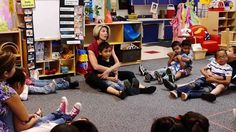 a group of children sitting on the floor in front of a woman talking to them