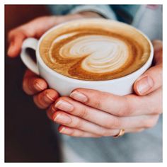 two hands holding a cup of coffee with latte art on the foam in it