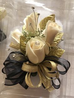 a white rose and black ribbon corsage in a clear plastic box with gold sequins