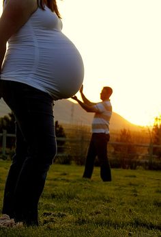 a pregnant woman holding a baseball bat in front of a man with his hand on the belly