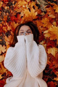 a woman covers her face with her hands while laying on the ground covered in leaves