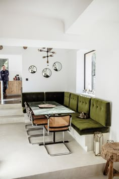 a green couch sitting next to a table in a living room under a clock mounted on the wall