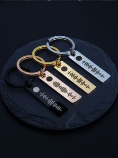 three different key chains sitting on top of a black stone circle with the words happy birthday written in gold, silver and black