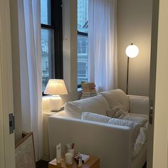 a living room with a white couch and table in front of the window, next to a lamp