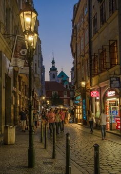 people are walking down the street in an old european city at night with lights on