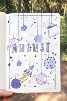 a hand holding an open notebook with space and stars on the pages that says august