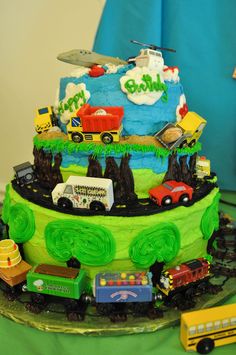 a birthday cake with cars and trucks on it is sitting on a green tablecloth