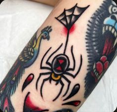 a close up of a person's arm with a spider and bird tattoos on it