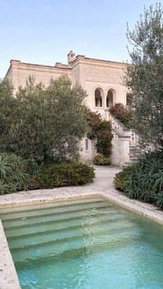 an outdoor swimming pool surrounded by greenery and trees in front of a large house