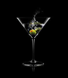 a martini glass filled with an olive and water splashing from the top to the bottom