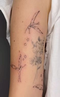 a woman's arm with tattoos on it and flowers in the air, flying around