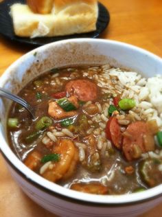 a bowl of soup with shrimp, rice and green peppers next to a loaf of bread