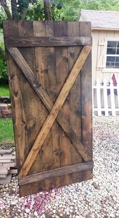 a large wooden gate sitting on top of a gravel covered ground next to a tree