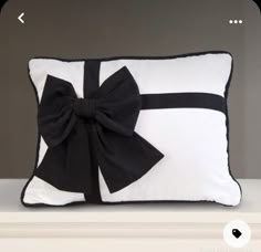 a black and white pillow with a large bow on it's side, sitting on a shelf