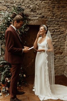 a bride and groom standing in front of a stone wall with greenery on it