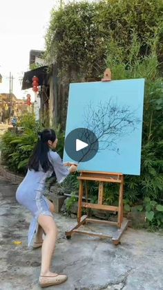 a woman standing in front of an easel with a painting on it's side