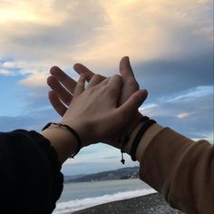 two people reaching out their hands to touch each other with the ocean in the background