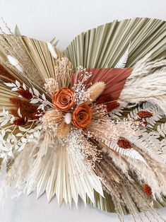 an arrangement of dried flowers and feathers on a white background with red roses in the center