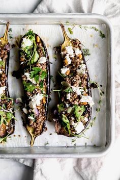 three stuffed eggplant halves on a baking sheet topped with feta cheese and cilantro