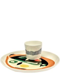 a white cup and saucer sitting on top of a multicolored plate with an abstract design